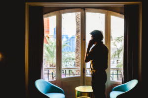 Silhouette of a man of the phone looking out the window from his home.